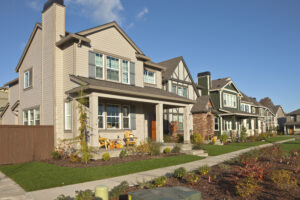 Row of suburban houses under a clear blue sky, featuring manicured lawns and autumn decorations on porches, evoking warmth and community.