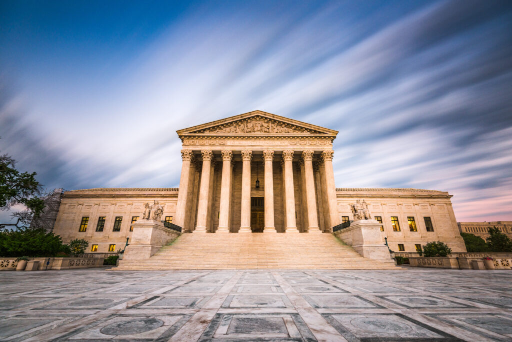 Grand, neoclassical building with tall columns and ornate pediment under a dynamic sky. The wide plaza enhances its imposing presence.